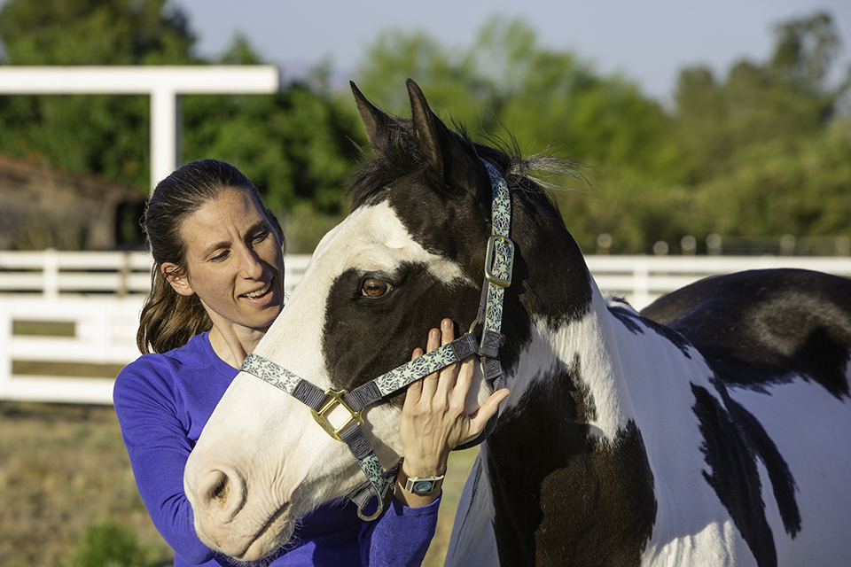 A woman in blue gently holding horses head